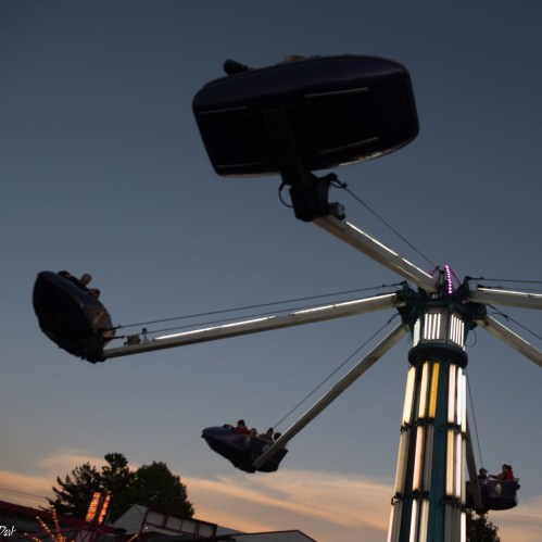 A swing ride at dusk with riders enjoying the view against a colorful sky.