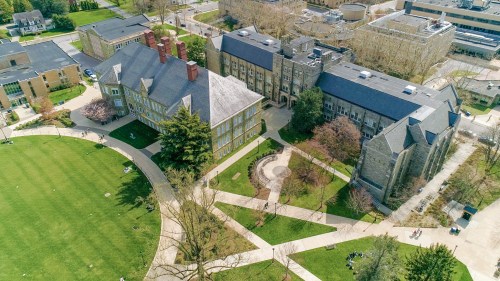 Aerial view of a campus featuring green lawns, pathways, and historic buildings surrounded by trees.