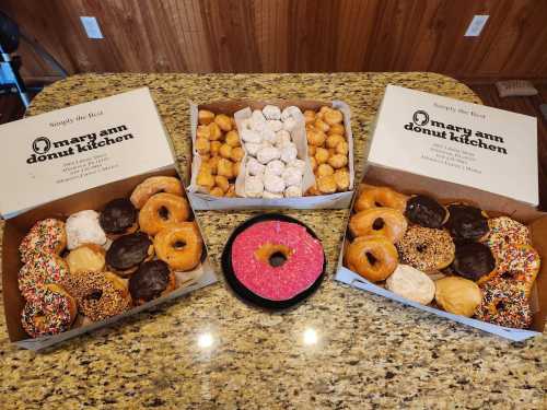 Three boxes of assorted donuts, including glazed, chocolate, and sprinkled varieties, on a granite countertop.