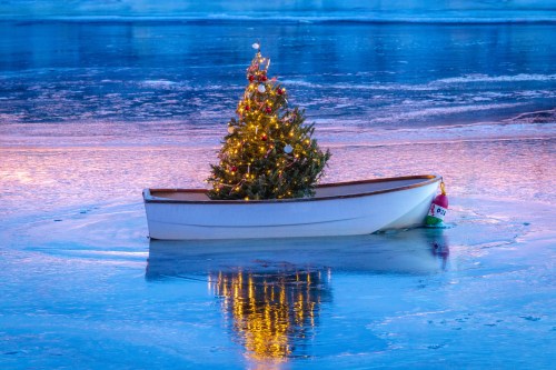 A small boat on icy water with a decorated Christmas tree, reflecting colorful lights in the serene winter scene.