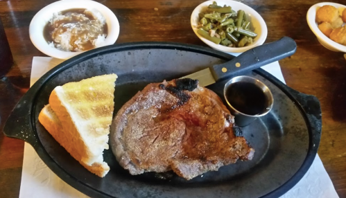 A sizzling steak on a plate with toast, gravy, green beans, and a side of mashed potatoes.