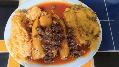 A plate of rice, topped with seasoned ground beef, plantains, and melted cheese in a savory sauce.