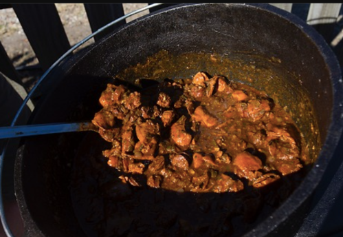 A large pot filled with a thick, savory stew containing chunks of meat and spices, sitting outdoors.