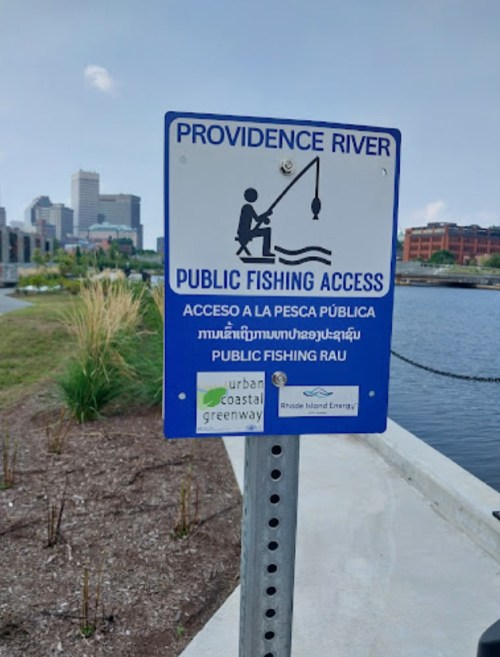 Sign indicating public fishing access at Providence River, featuring multiple languages and urban scenery in the background.