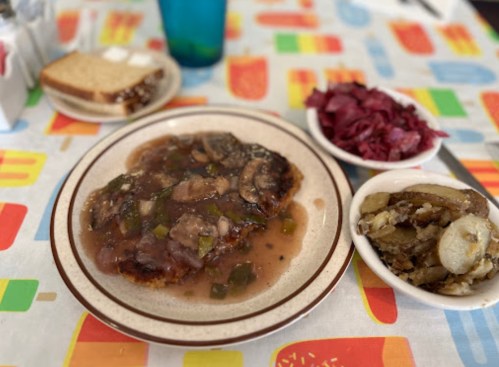 A plate of chicken with mushroom sauce, served with pickled red cabbage and a side of sautéed vegetables, on a colorful tablecloth.