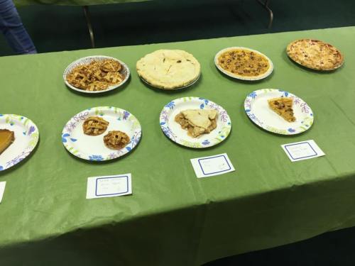 A table with various desserts on paper plates, including pies and slices of baked goods, set on a green tablecloth.