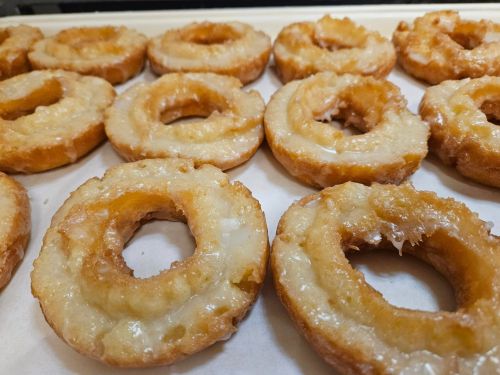 A close-up of freshly glazed donuts arranged on a tray, showcasing their golden-brown color and shiny glaze.