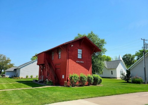 A bright red two-story building with a staircase, surrounded by green grass and trees under a clear blue sky.
