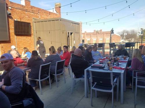 A lively rooftop restaurant scene with diners at tables, enjoying food and drinks under string lights.