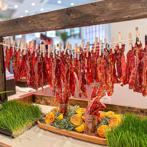 A display of hanging strips of cured meat, garnished with herbs and orange slices, on a wooden stand.