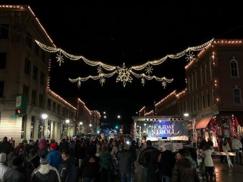 A festive street scene at night, bustling with people under twinkling holiday lights and decorations.
