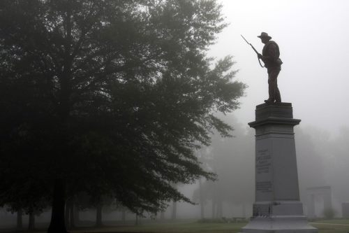 A foggy scene featuring a soldier statue atop a pedestal, surrounded by trees in a cemetery.