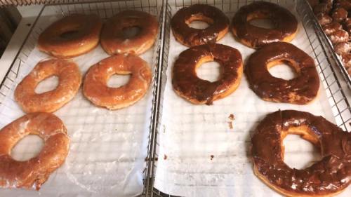 A tray of freshly baked donuts, some glazed and others chocolate-covered, arranged on parchment paper.