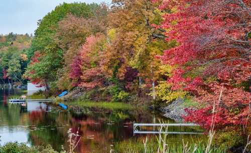 A serene lake surrounded by vibrant autumn foliage in shades of red, orange, and yellow, reflecting on the water.