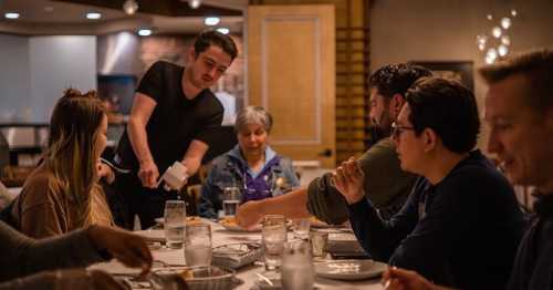 A waiter serves food to a group of people dining together at a restaurant table, enjoying a meal and conversation.