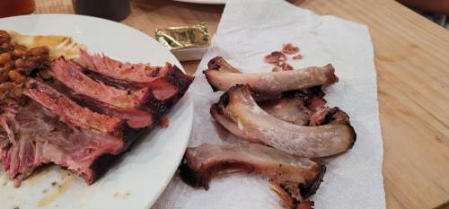 A plate with leftover ribs and a side of baked beans, with some discarded rib bones on a paper towel.