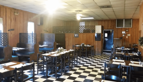 Cozy restaurant interior with wooden walls, checkered floor, and booths, featuring tables set for dining.