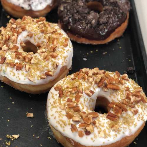 A tray of assorted donuts: two with white icing and pecans, one chocolate, and one with a crumb topping.