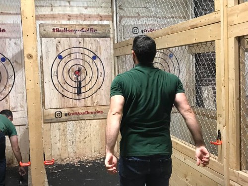 A person stands in an axe throwing venue, facing targets with bullseyes, ready to throw an axe.