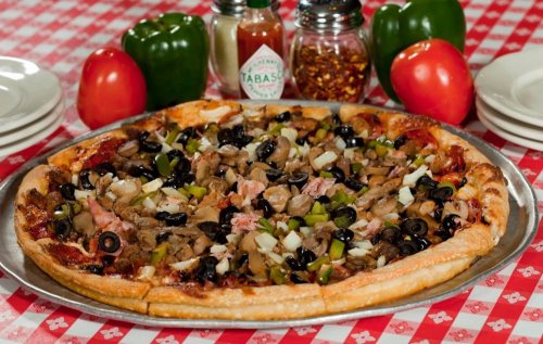 A large pizza topped with mushrooms, olives, green peppers, and onions, surrounded by condiments and fresh vegetables.