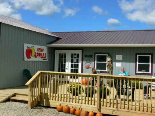 A rustic building with a "Fresh Apples" sign, featuring a wooden deck and pumpkins in front, under a blue sky.