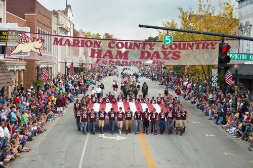 A parade in Lebanon, KY, with a large banner reading "Marion County Country Ham Days" and crowds lining the street.