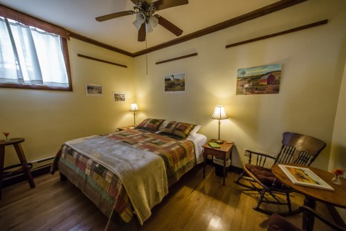 Cozy bedroom with a quilted bed, wooden furniture, and soft lighting from lamps, featuring artwork on the walls.