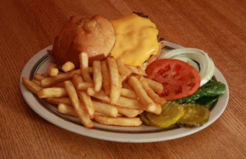 A plate with a cheeseburger, lettuce, tomato, pickles, and a side of French fries.