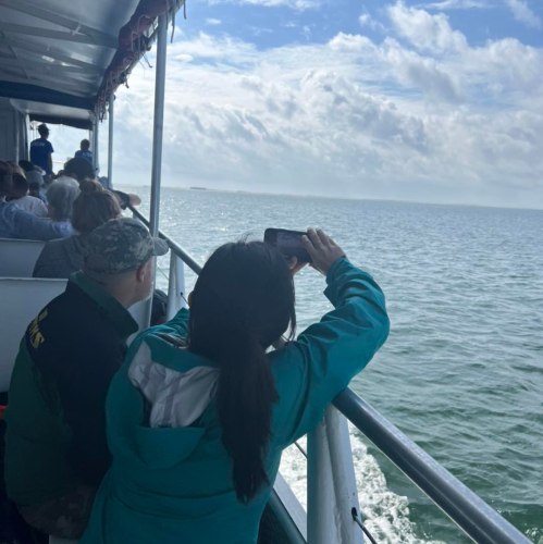 A group of people on a boat, with one person taking a photo of the ocean and distant land.