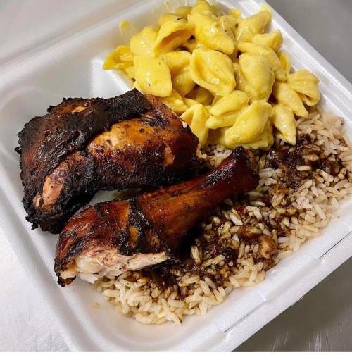 A takeout container with grilled chicken, seasoned rice, and creamy macaroni and cheese.