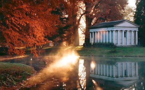 A serene landscape featuring a classical building by a misty pond, surrounded by vibrant autumn foliage.