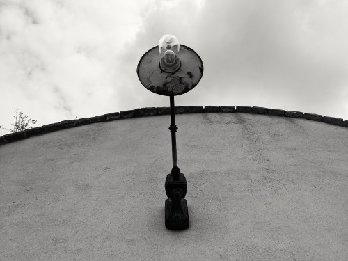 A vintage wall lamp mounted on a textured wall, with a cloudy sky in the background.