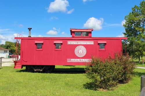 A red caboose with "Withlacoochee State Trail" written on it, set against a blue sky and green grass.