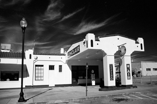 Black and white image of a vintage Sinclair gas station with distinctive architecture and a clear sky.