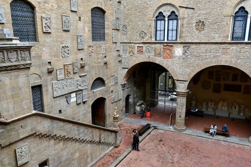 A historic courtyard with arches, stone walls, and sculptures, featuring visitors exploring the space.