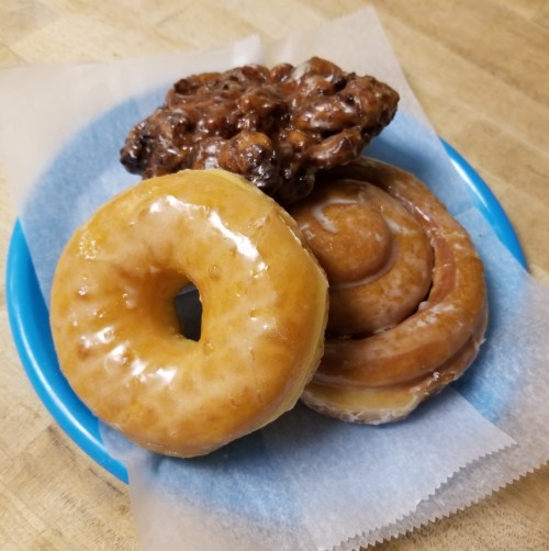 A blue plate with three types of donuts: a glazed ring, a cinnamon roll, and a chocolate-covered fritter.