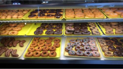A display case filled with various donuts, including glazed, chocolate, and sprinkled varieties on yellow trays.