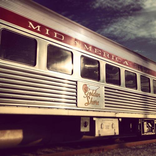A vintage train car with "Mid America" and "Golden Shore" signage, set against a cloudy sky.