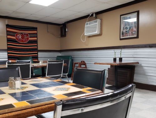 A cozy restaurant interior with wooden tables, chairs, and decorative wall art, featuring an air conditioning unit.