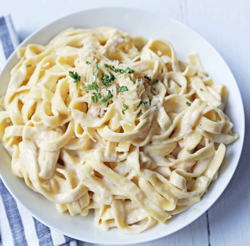 A plate of creamy fettuccine pasta topped with grated cheese and herbs, served on a white wooden surface.