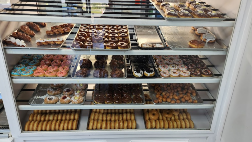 A display case filled with various types of colorful donuts and pastries on multiple trays.