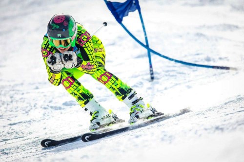 A skier in a bright neon outfit races down a snowy slope, focused and in motion.
