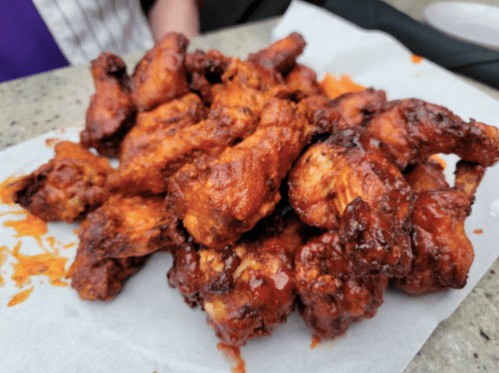 A pile of saucy, crispy chicken wings on a white paper plate, with some cheese sprinkled on top.