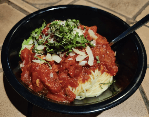 A bowl of spaghetti topped with marinara sauce, chopped herbs, and onions, served with a fork.