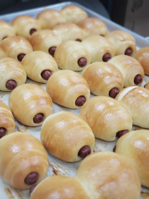 A tray of golden-brown bread rolls with hot dogs peeking out, arranged neatly in rows.