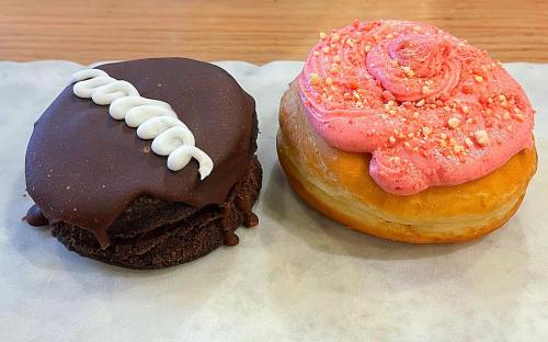 Two colorful donuts: one chocolate with white icing and one with pink frosting and sprinkles on a light background.