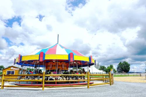 A colorful carousel with a striped canopy, surrounded by a wooden fence, set against a cloudy sky.