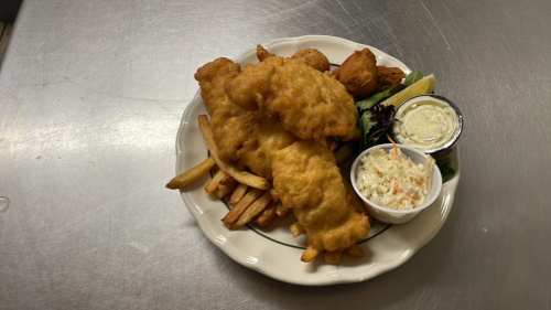 A plate of fish and chips featuring battered fish, fries, coleslaw, and dipping sauces, garnished with lemon.