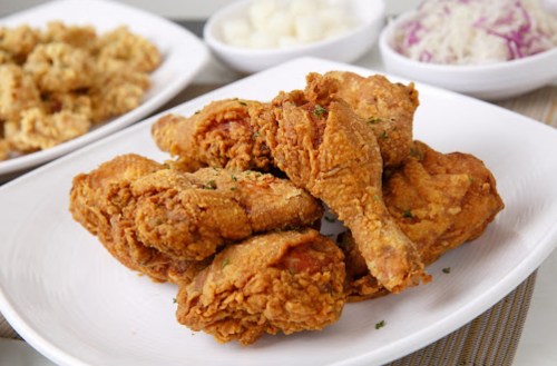 A plate of crispy fried chicken pieces, garnished with herbs, alongside bowls of side dishes.