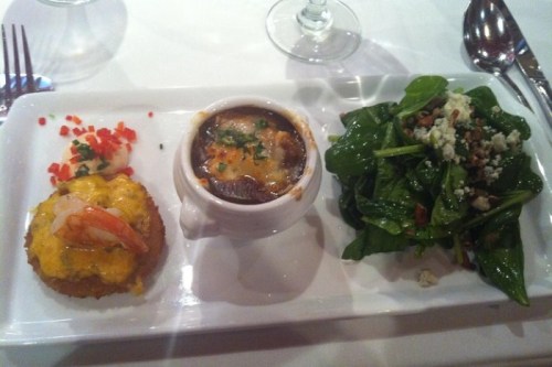 A plate with a shrimp dish, French onion soup, and a spinach salad with nuts and cheese.